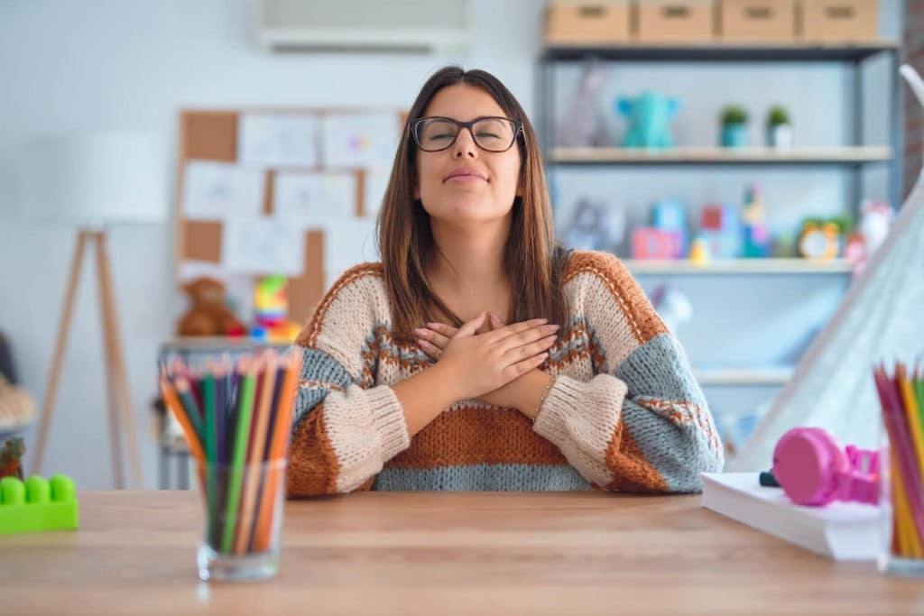 Young teacher sitting at a desk with her eyes closed.