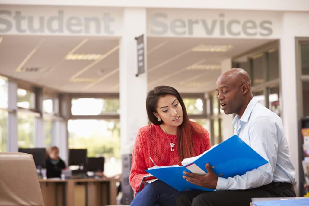A man holding an open binder talking to a woman.