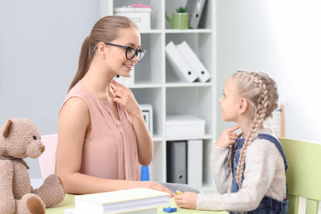 Speech therapist working with a young girl at a table.