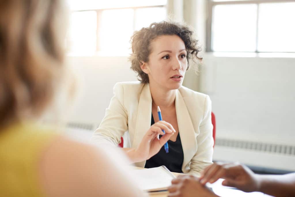 Professional woman sitting at a table with other adults with paper and a pen.