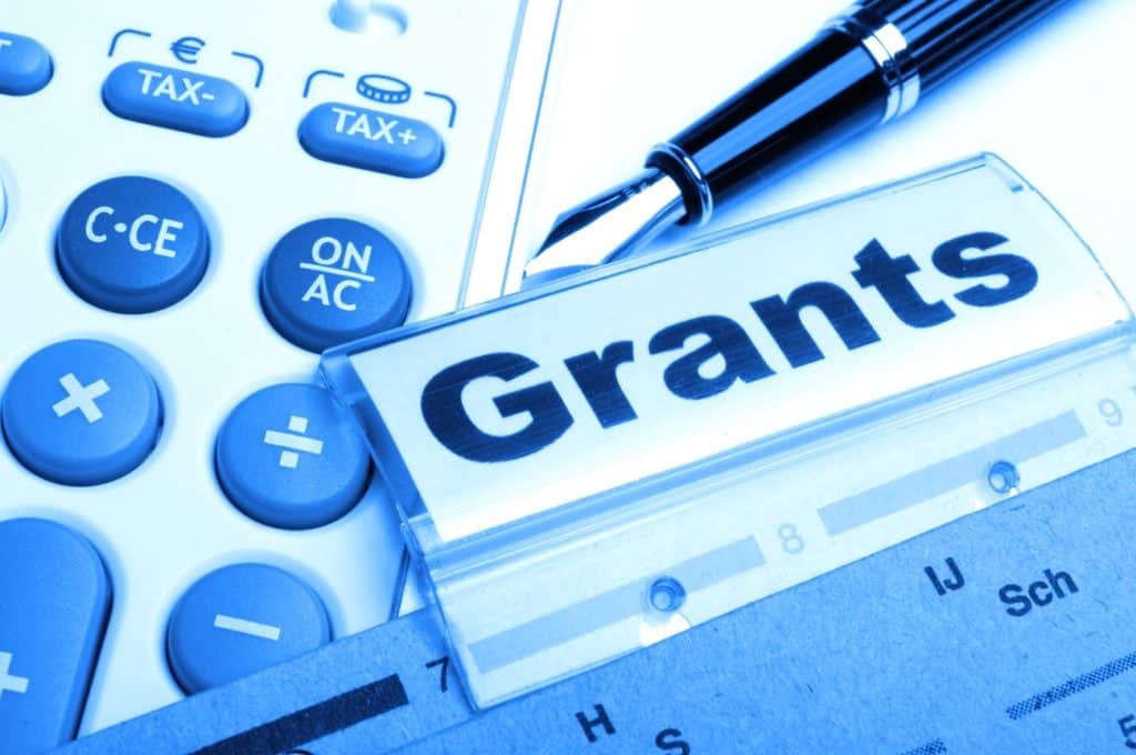 File folder labeled ‘Grants’ next to a calculator and pen.