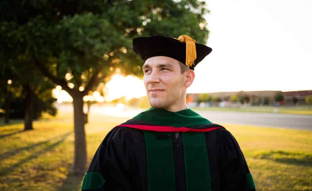 A man stands smiling in his doctorate cap and gown.
