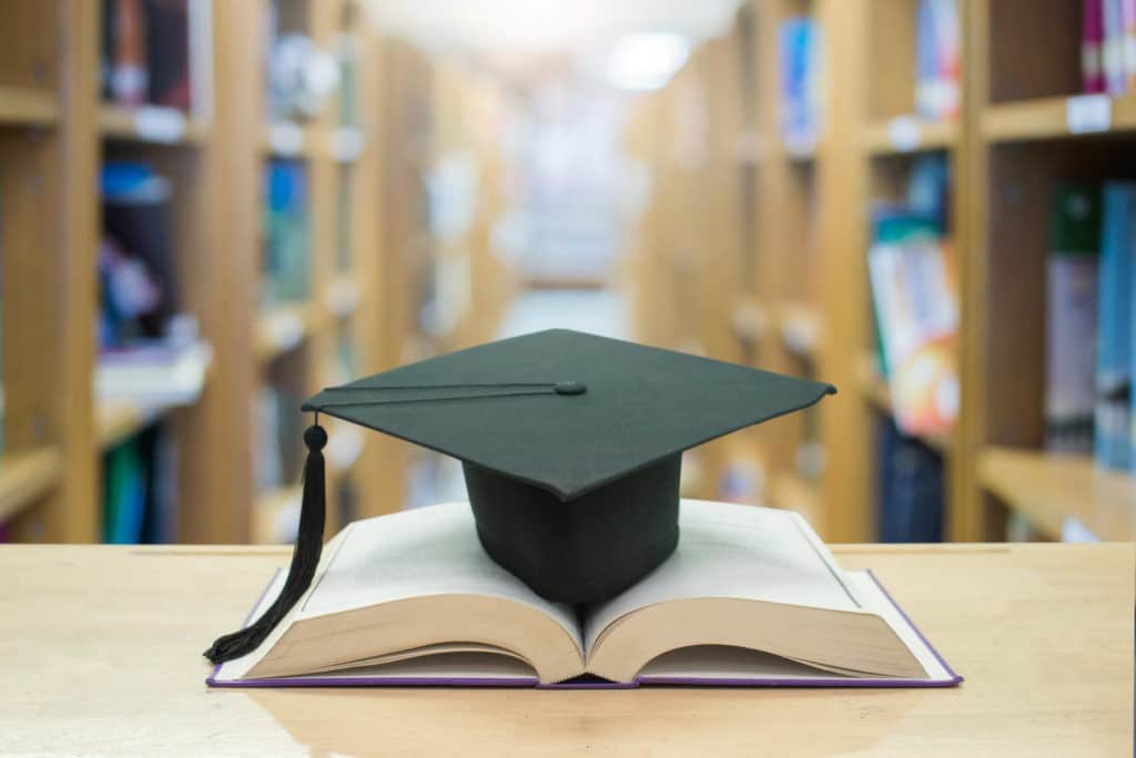Graduation cap sitting on top of an open book in a library.