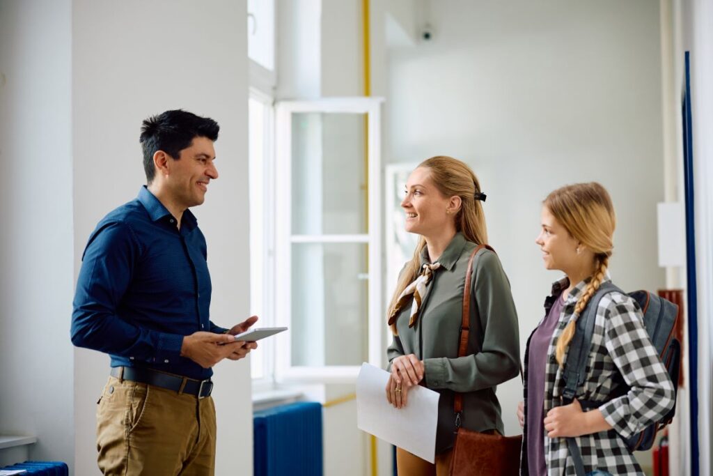 Back to school night: a teacher talks with a student and her mother in his classroom.
