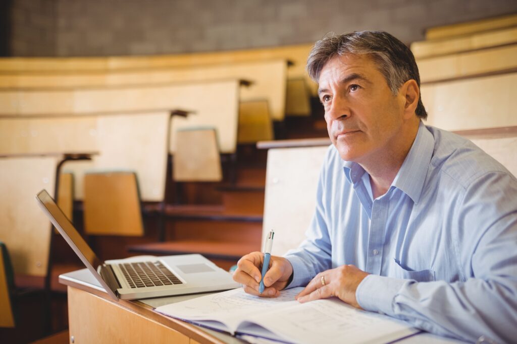 A teacher attends a college class and sits in a lecture hall.