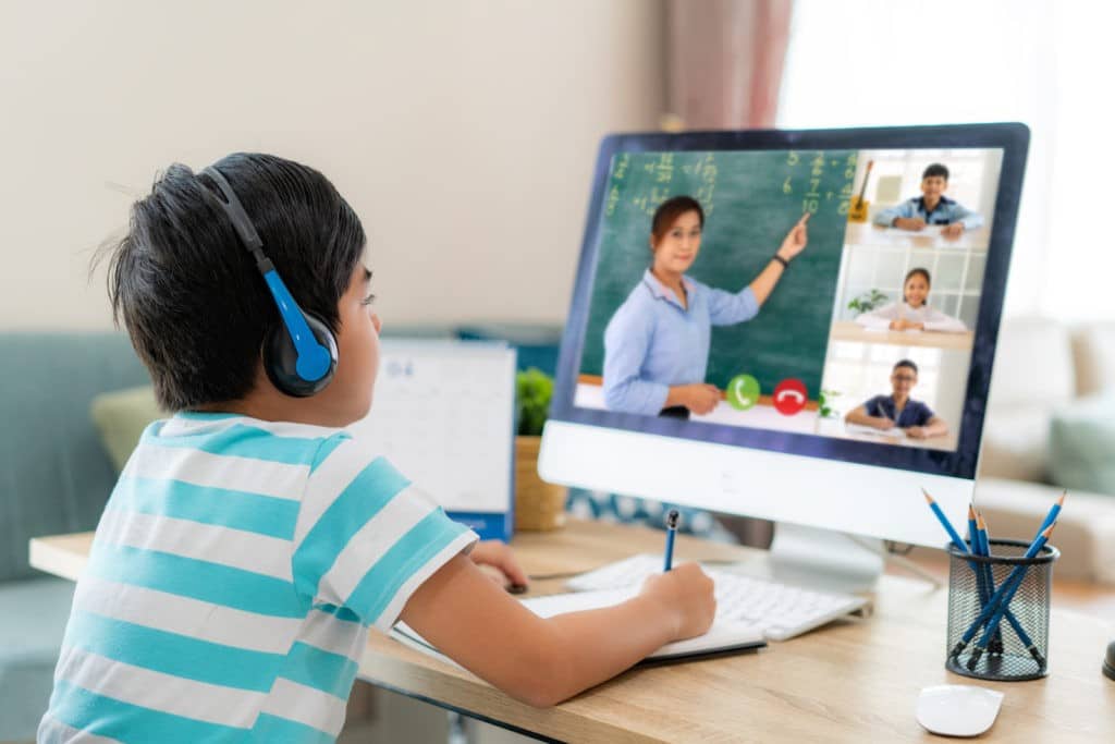 Young boy wearing headphones during a Zoom lesson with a teacher.