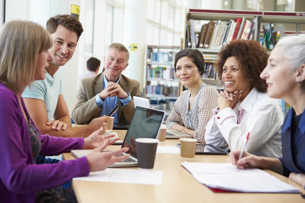 Group of teachers sitting at a table in a library talking.