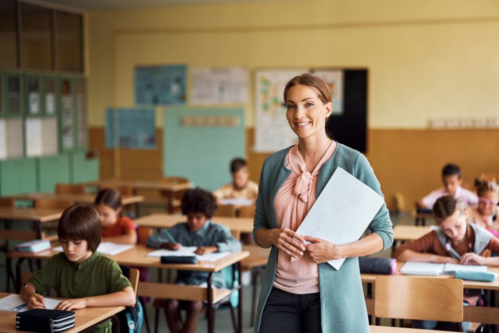 A portrait of a smiling teacher standing in front of her classroom.