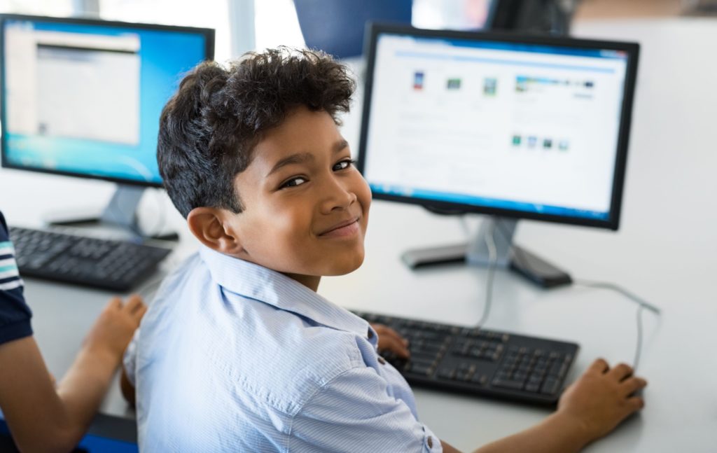 Young boy smiling while working on a desktop computer.