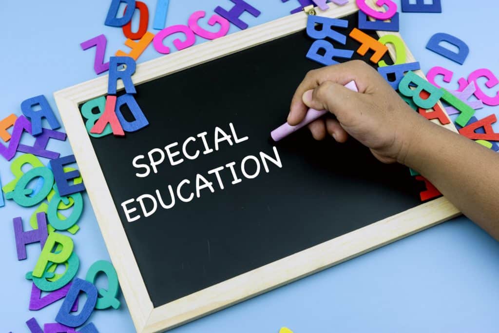 Close up of a student hand writing “special education” on a chalkboard with piles of letters surrounding it.