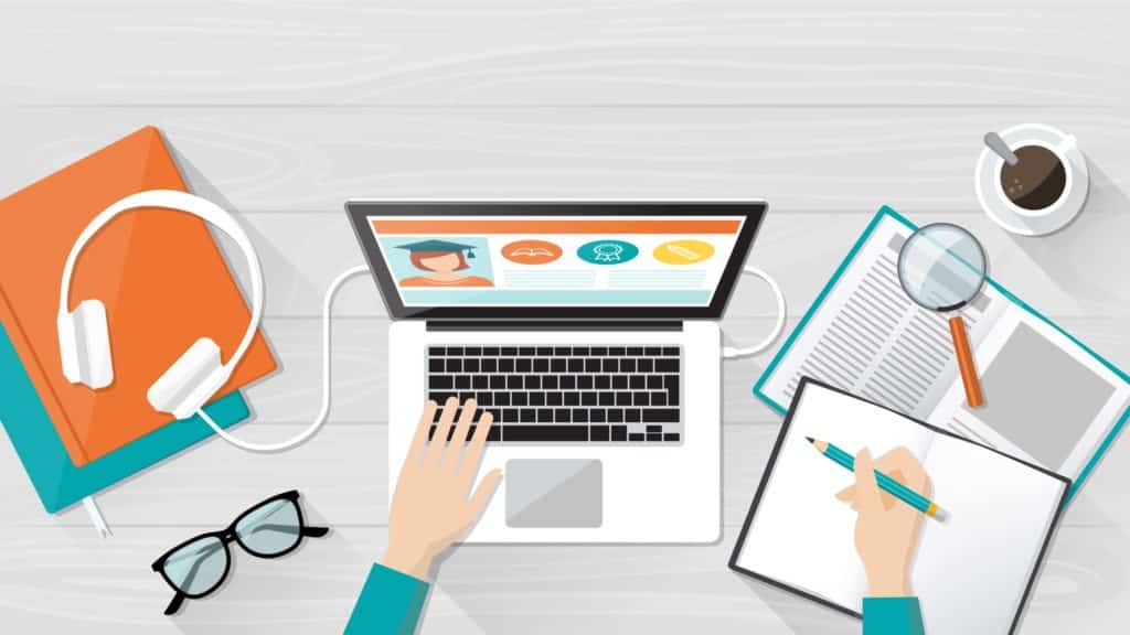 A student sitting at a table using a laptop and taking notes.