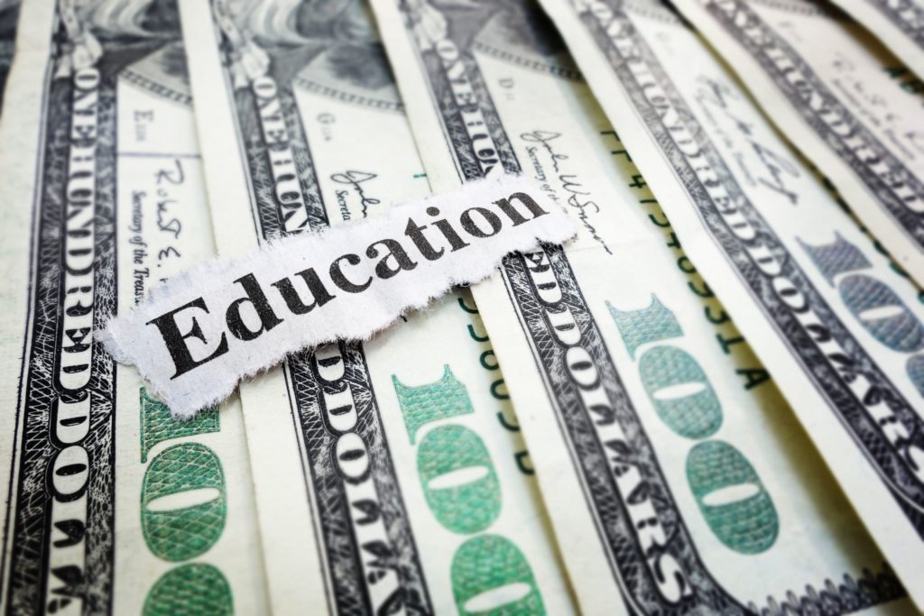 A close-up of hundred dollar bills with a cut-out of the word education” laying on top.