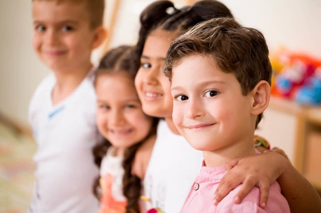 Small group of students in a classroom embracing each other and smiling.