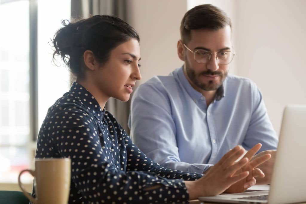 Woman sitting at a desk with a colleague showing him something on a laptop.