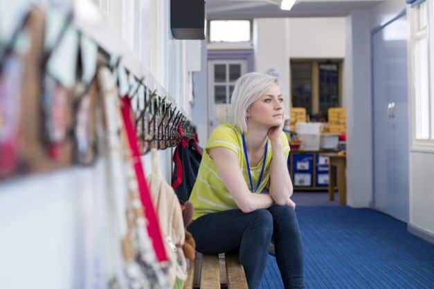 A teacher sits on a bench in school; she is looking pensively out of the window.