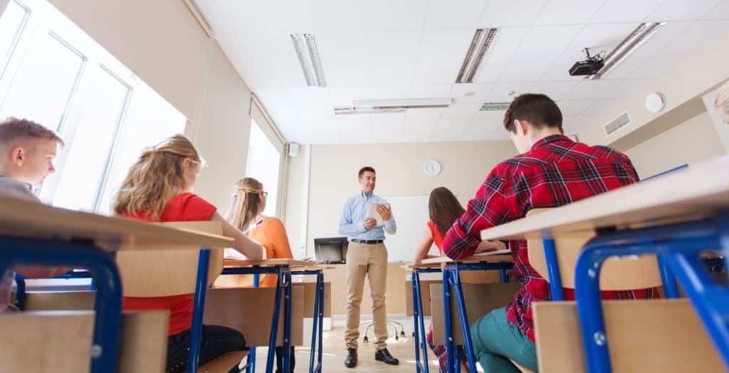 Male teacher standing at the front of a classroom lecturing to students.