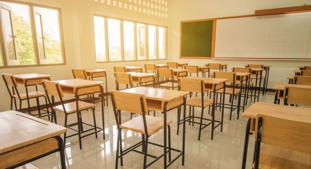 A classroom sits empty with the sun shining in the window.