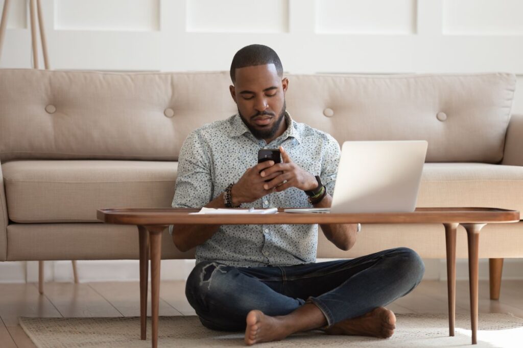 A man working on his laptop, checks his phone, looking distracted.