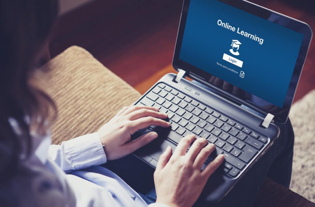 Woman sitting using a laptop with online learning on the screen.
