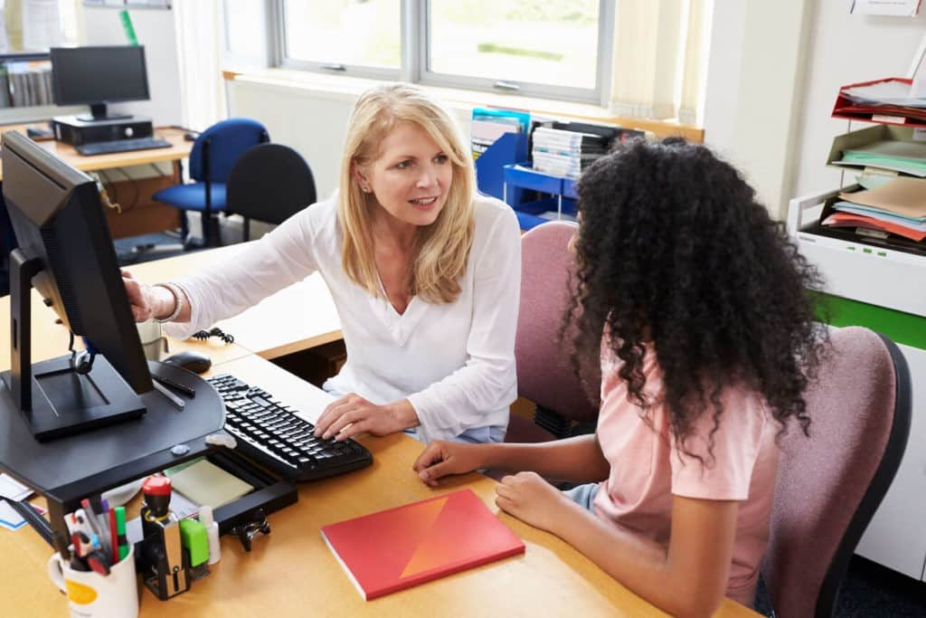 An academic advisor sitting with a student and pointing something out on the computer.
