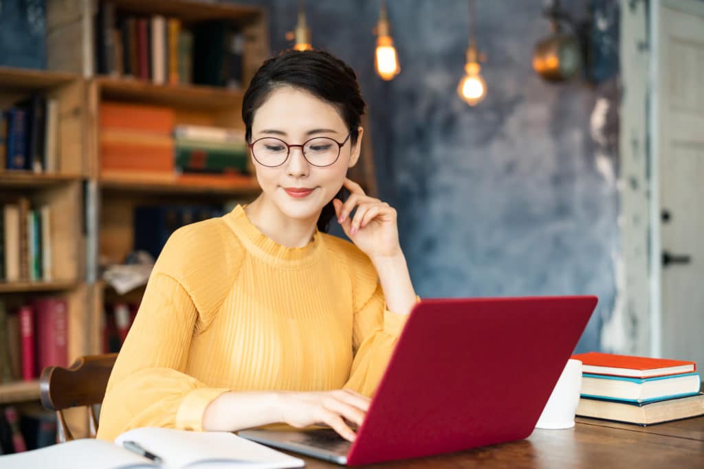 Young women sitting at a table with books working on a laptop.