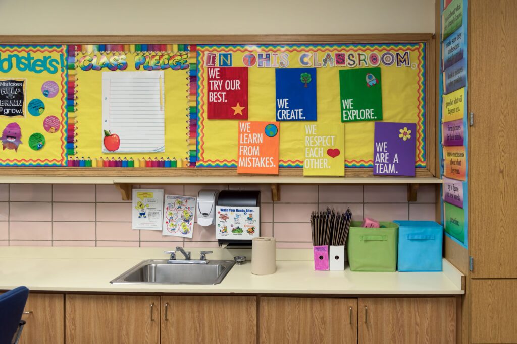 A bulletin board with bright and colorful bulletin board decorations above the sink in an elementary school classroom.