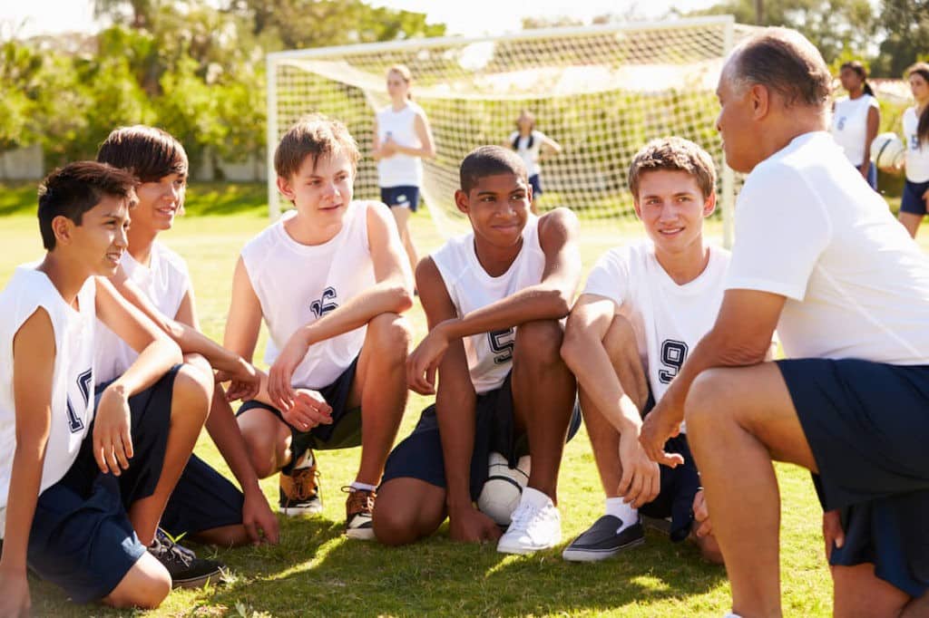 Coach kneeling on the ground and talking with his soccer team.