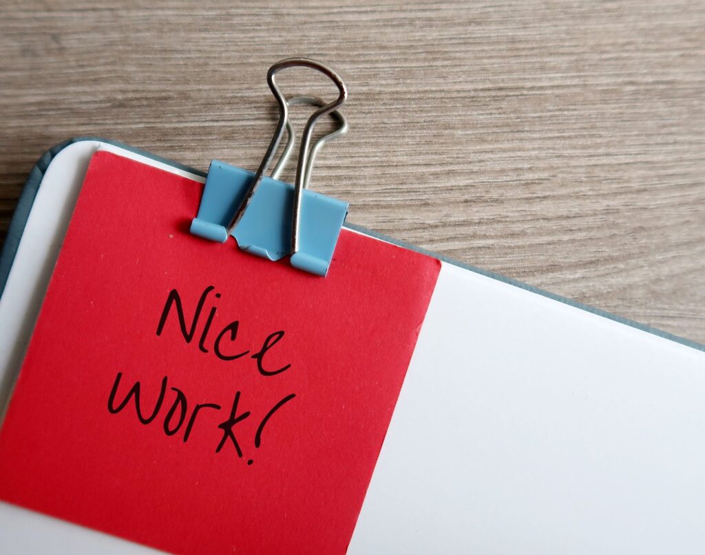 A staff appreciation Post-It note with “nice work!” written on it is paper clipped to a document.