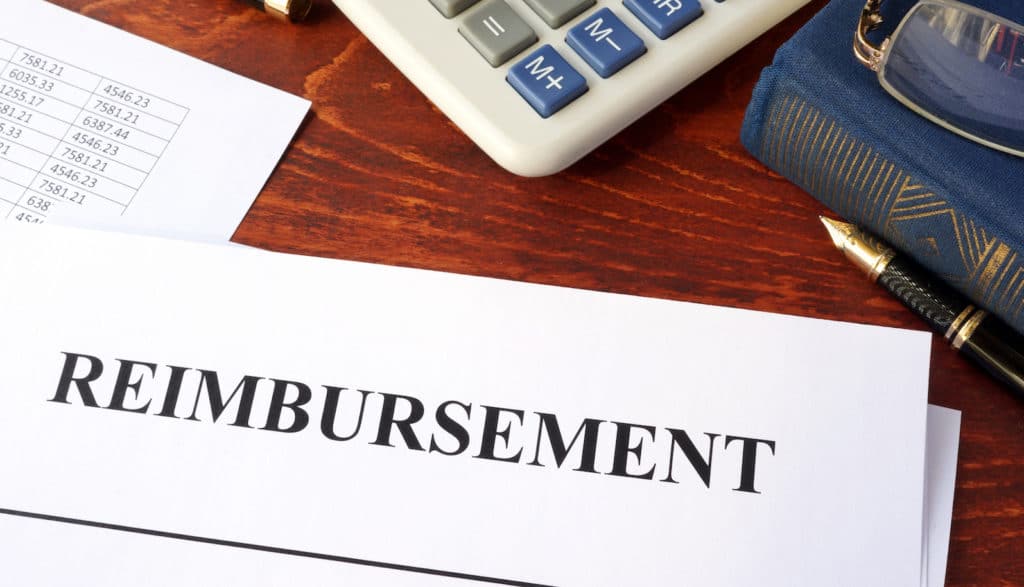 Document titled ‘reimbursement’ sitting on a table with a calculator, a pen, and glasses.