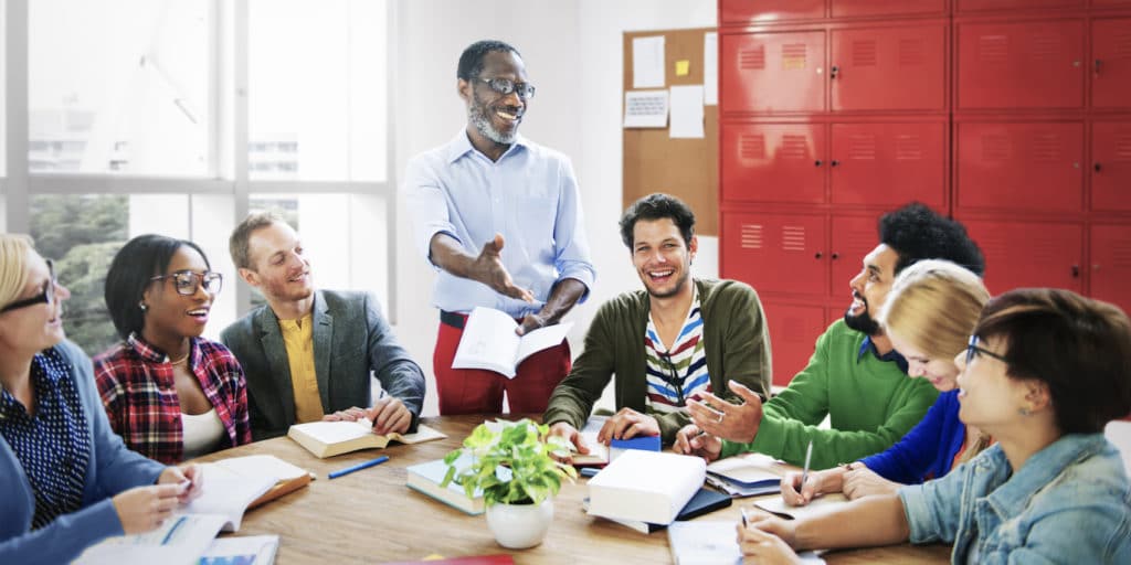 Group of adults sitting around a table with one person standing and speaking.