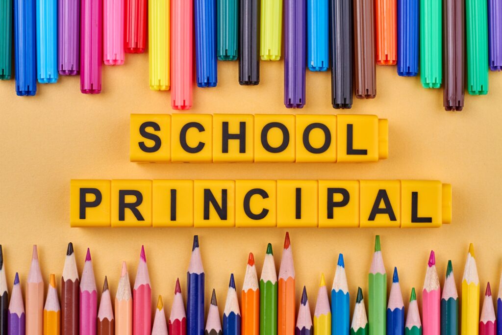 Yellow cubes spell out “school principal.” Colorful pencils and felt pens surround the cubes.