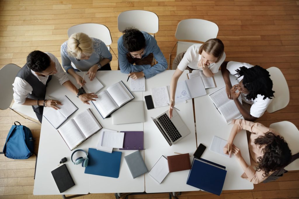 A group of college students works on homework around a table, books scattered between them.