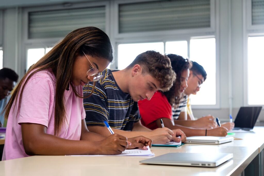 A portrait of students sitting at their desks, taking notes in their notebooks.