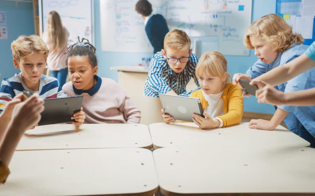 Group of students gathered around desks looking at laptops.