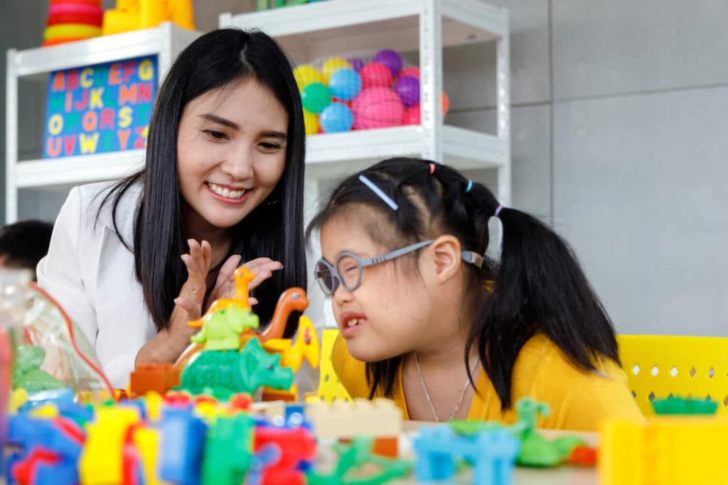 Teacher sitting at a table with a student with special needs playing with toys.