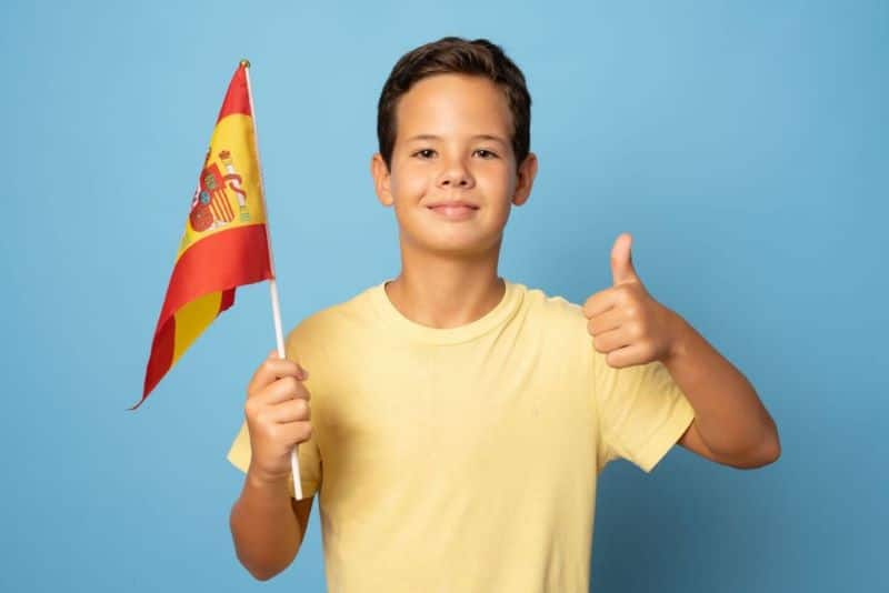 A boy holds the Spain flag, doing a thumbs-up.