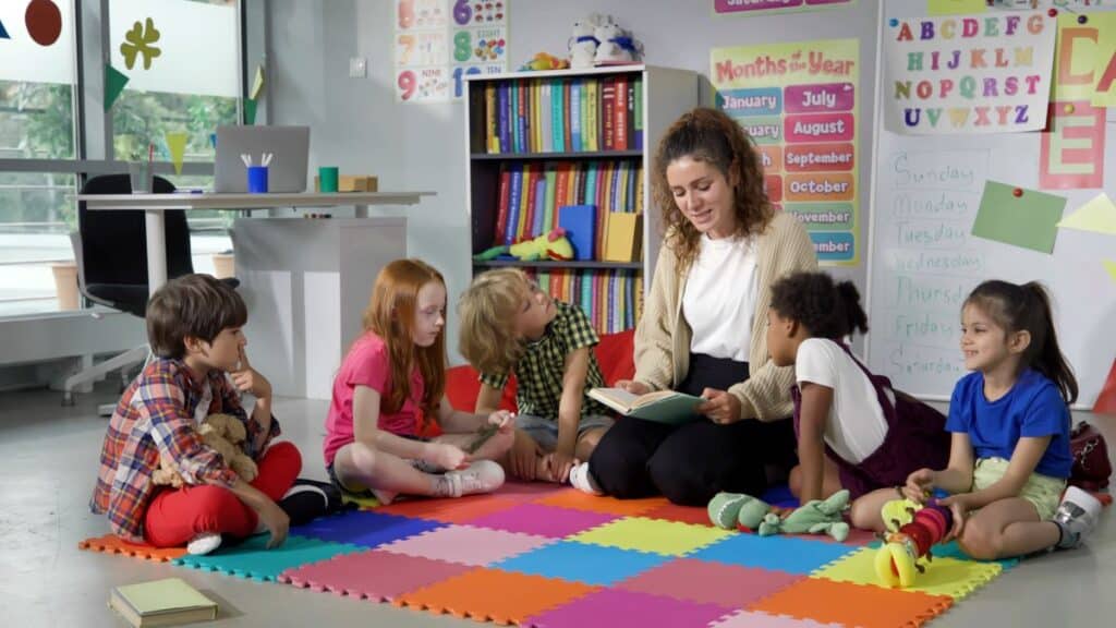 A kindergarten teacher sits with her students and reads to them.