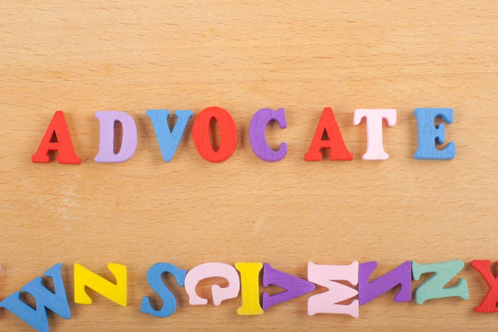 Wooden letters spell out the word “advocate” on a wooden table.