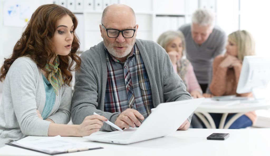 Older man mentoring a younger woman working on a laptop.