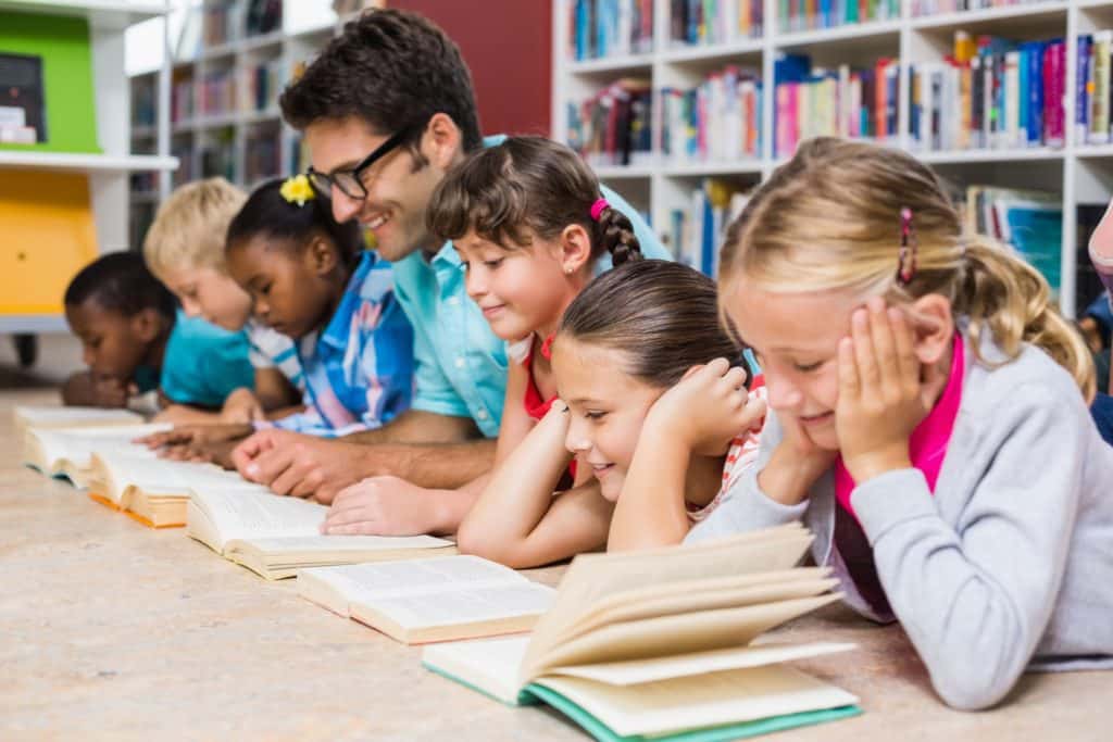 A teacher and his students lay on the library floor doing independent reading.