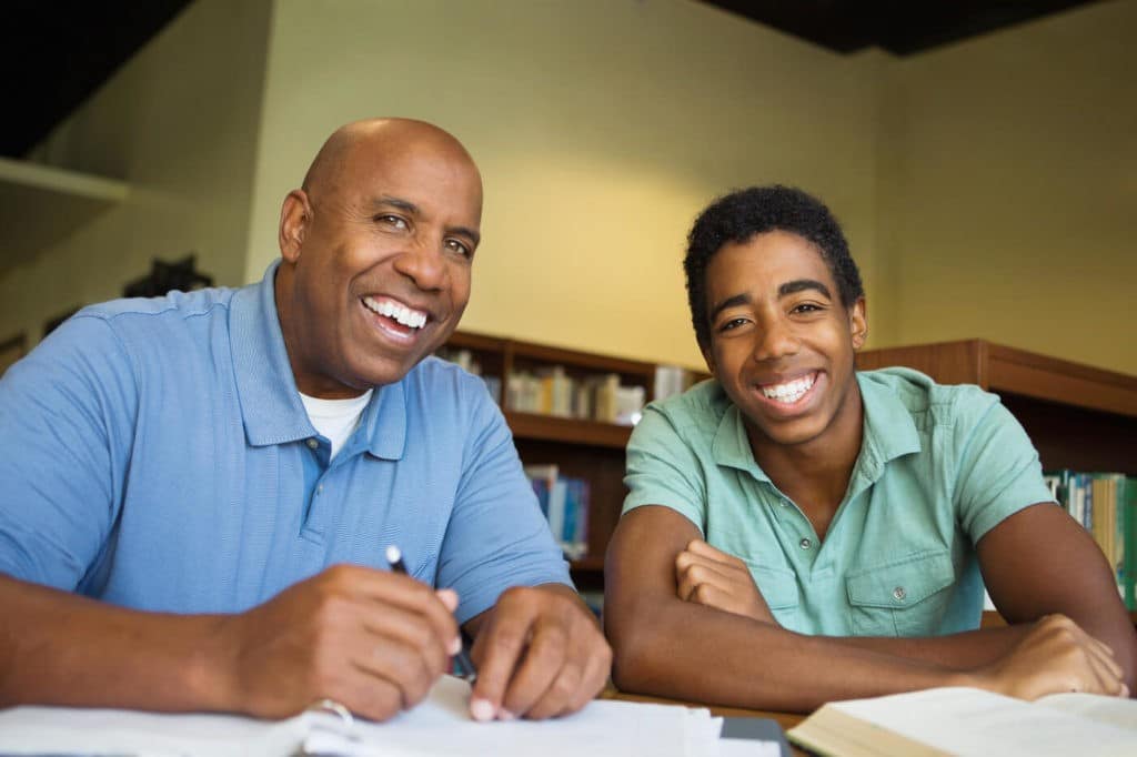 A teacher and student sit together in the library, surrounded by books and notebooks.
