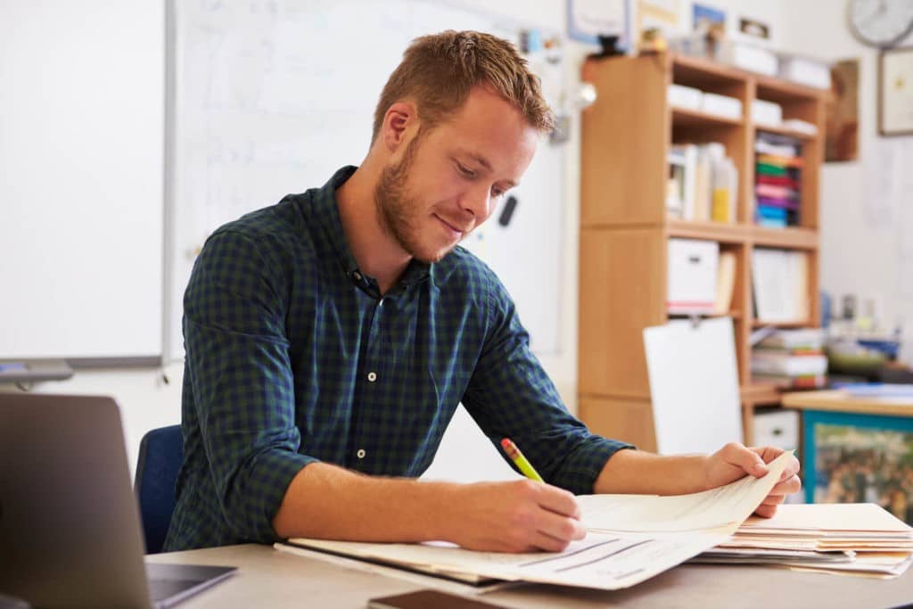 Young teacher sitting at his desk taking notes.