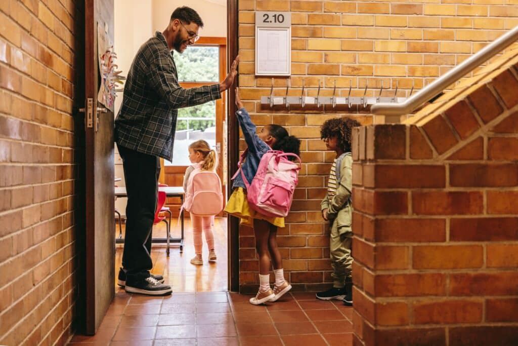 A teacher high-fives his students as they come in to the classroom.