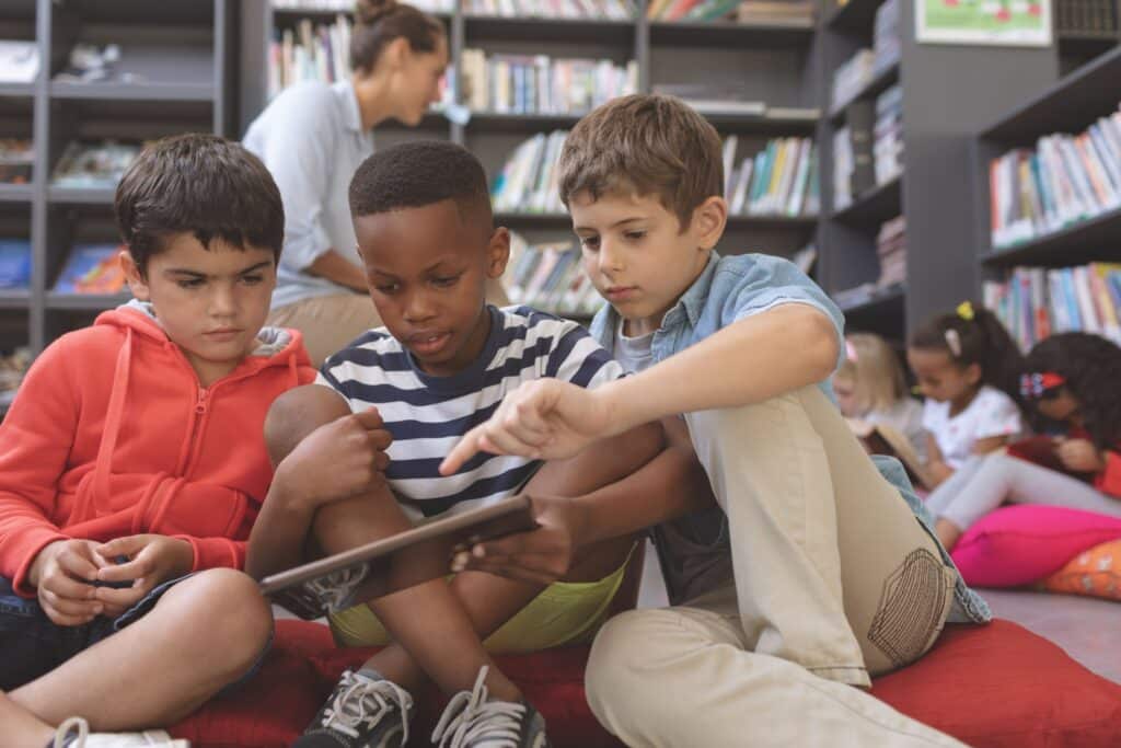 Three students use their tablet to read an E-book in the library.