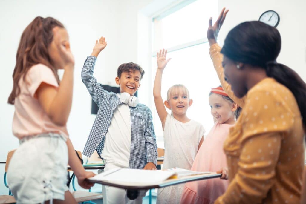 A group of happy elementary school children raise their hands with their teacher to high-five.