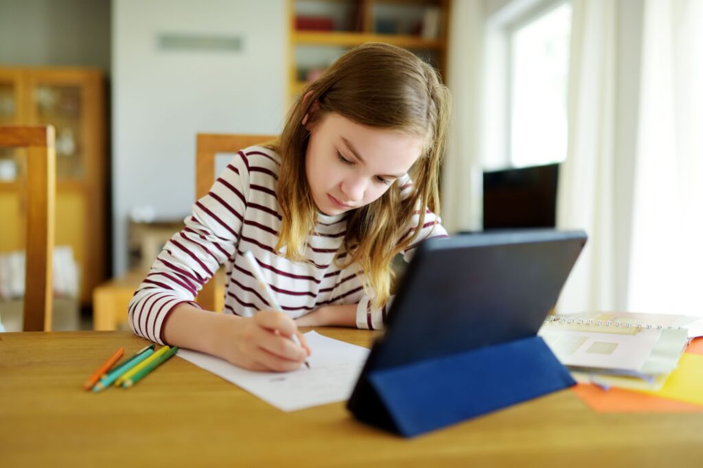 A pre-teen student sits at home doing her homework on her tablet.