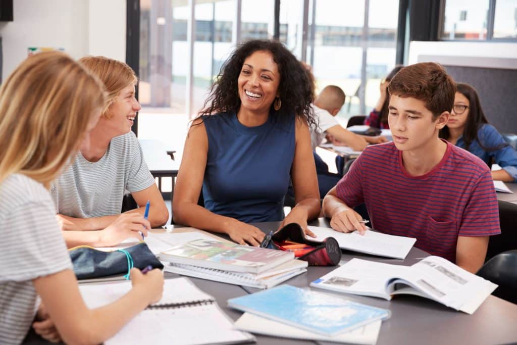 Teacher sitting with students at a table working.