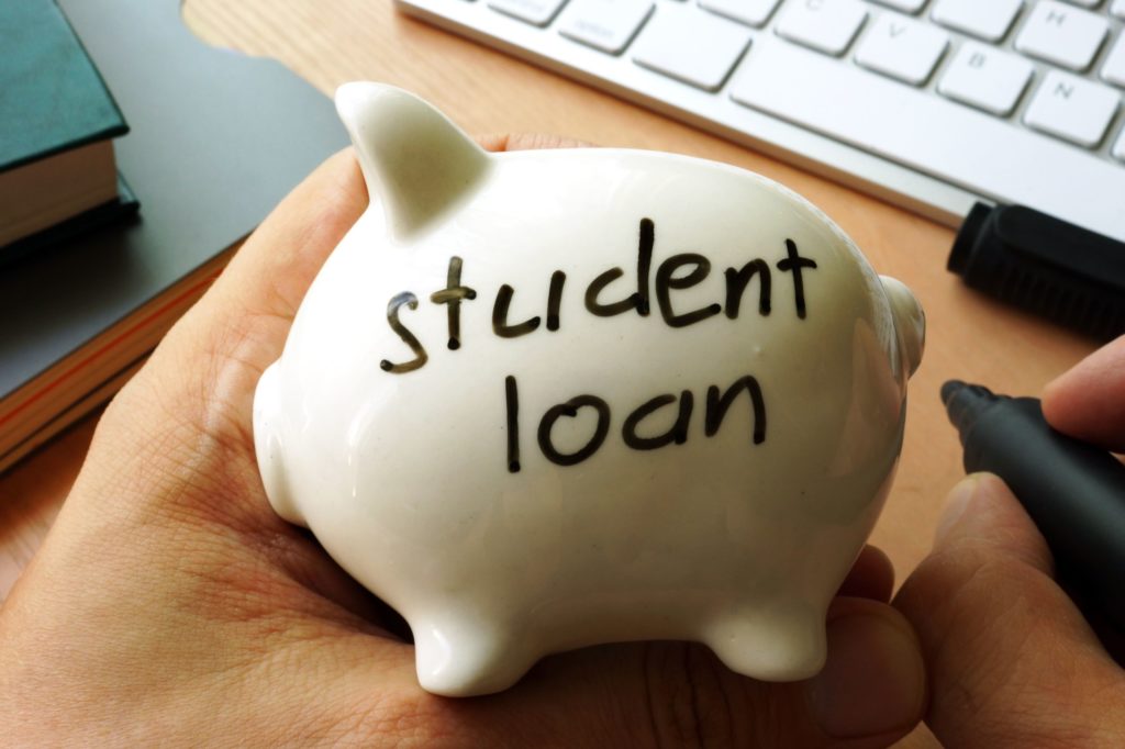 Person holding a piggy bank with the words student loan written on it.