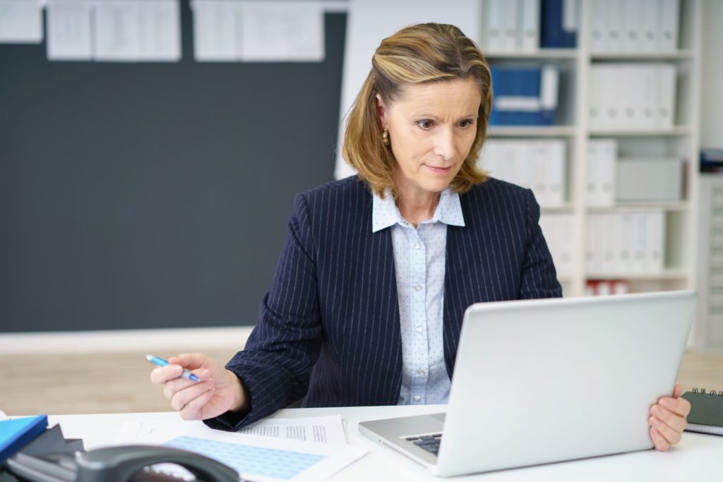 Woman holding pen and looking at laptop computer