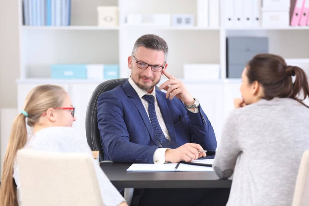 School principal sitting at his desk across from a parent and a student.